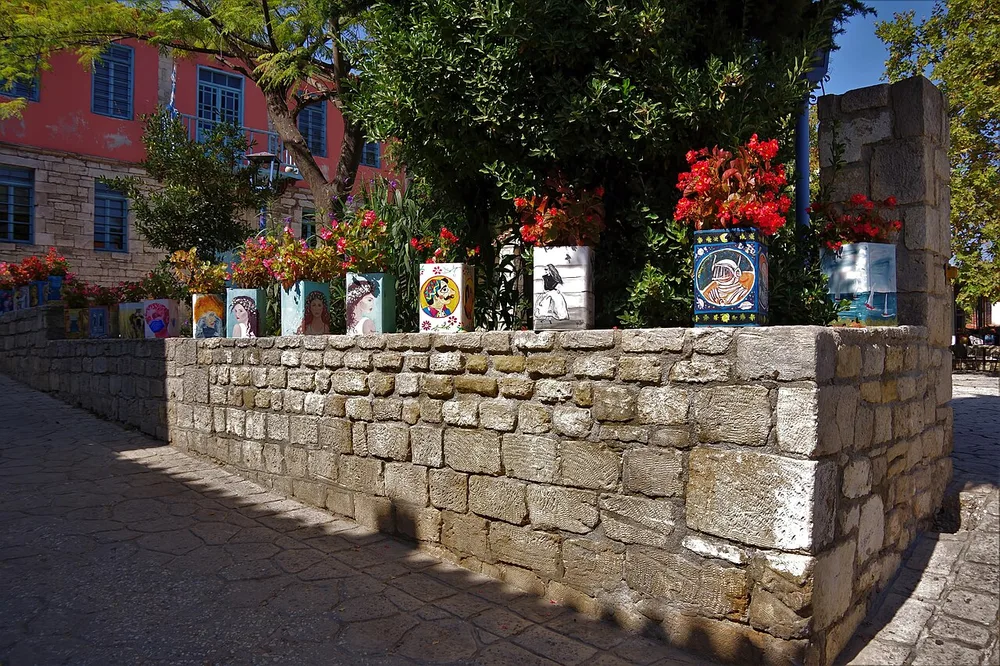 Painted flowerpots along a stone wall beside a traditional building with blue shutters in Afytos.