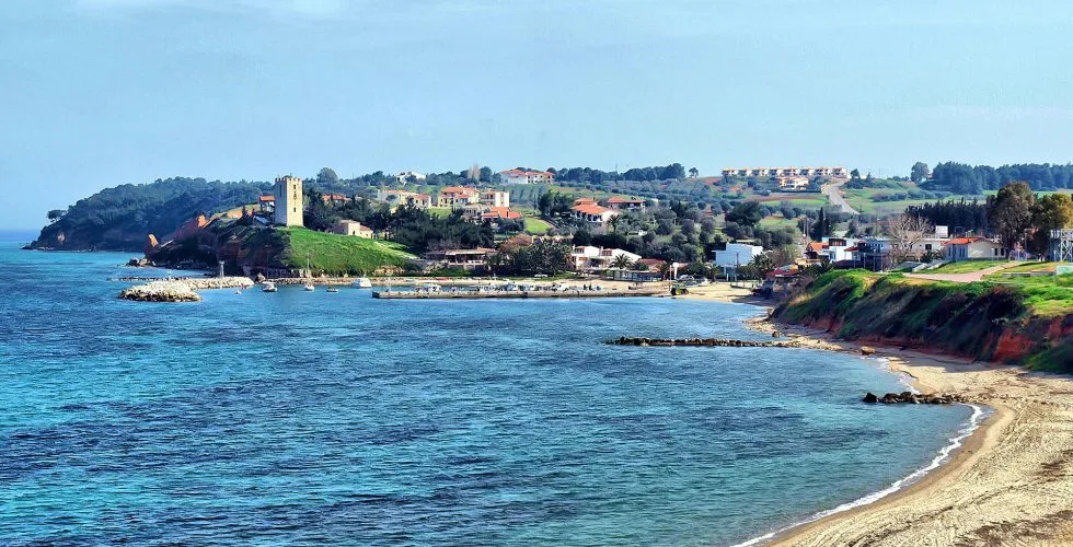 Nea Fokea waterfront with a sandy shoreline, harbour and stone tower above the sea.