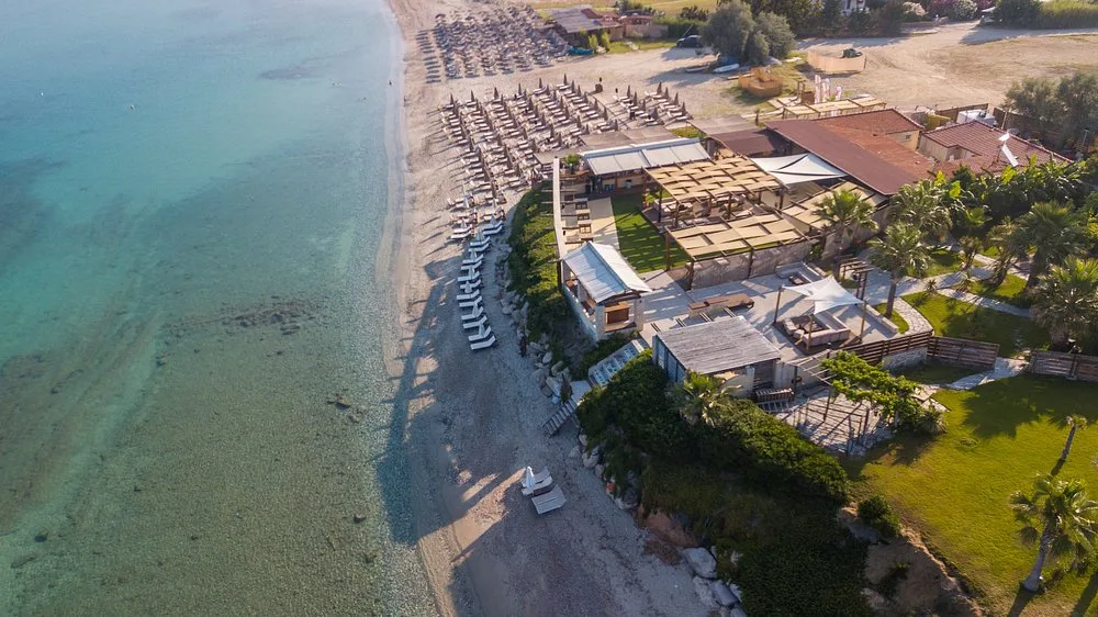 Aerial view of Zattero Seaside Bar with beach loungers, wooden terraces and clear water in Fourka.